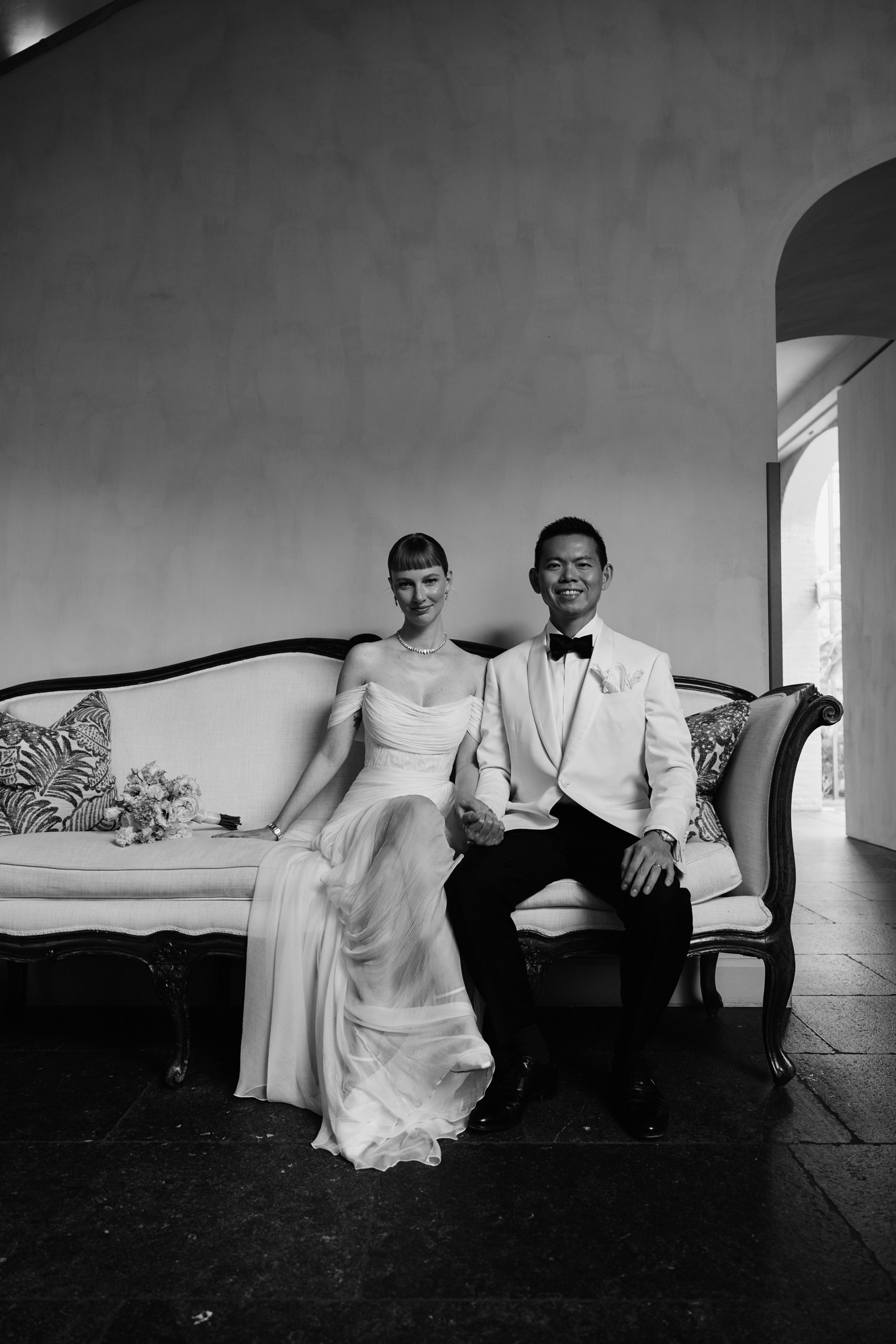 Lina and Jin holding hands on a sofa on their wedding day